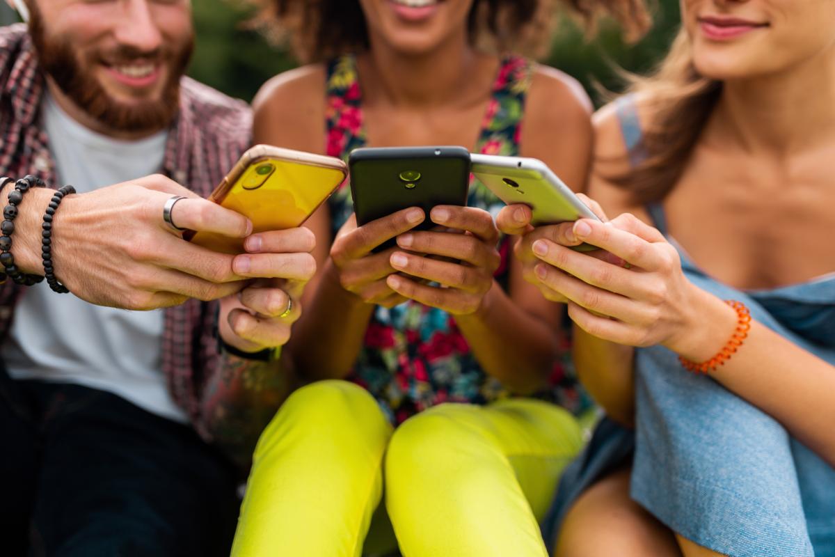 drie mensen glimlachen en kijken op hun gsm's