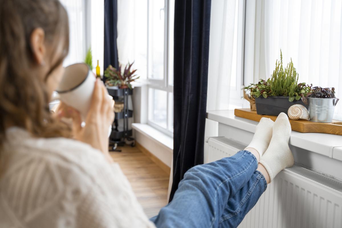 een vrouw zit in haar woning en verwarmt haar voeten aan een radiator