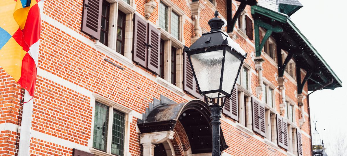 deteilfoto van de voorgevel van het gemeentehuis, met lichte sneeuw, een lantaarpaal en de vlag van de provincie Antwerpen
