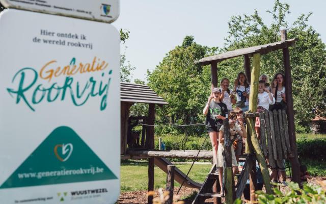 Een groepje kinderen aan het speelpleintje bij het Huis van het Kind, naast het infobord van Generatie Rookvrij