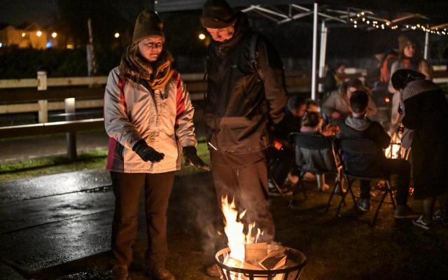 Enkele wandelaars verwarmen zich aan een vuurkorf tijdens de kerstwandeling van 2022