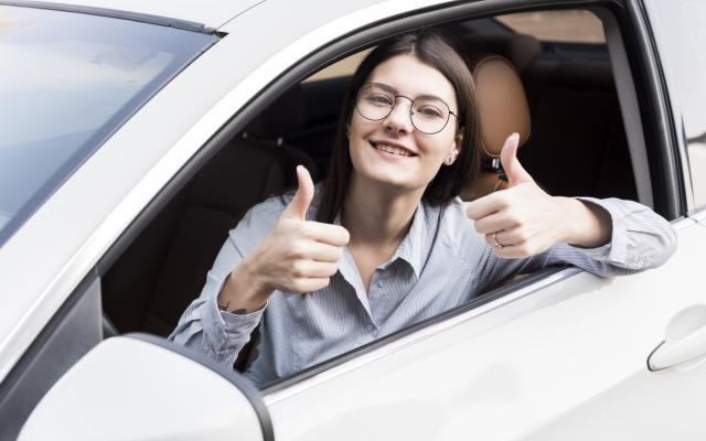 jonge vrouw in een auto toont haar twee duimen door het geopende venster