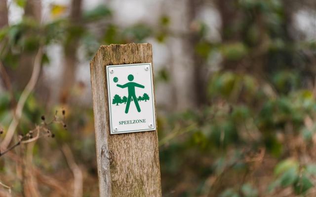 infopaaltje met een pictogram van een spelend kind in een bos, daaronder het opschrift 'speelzone'