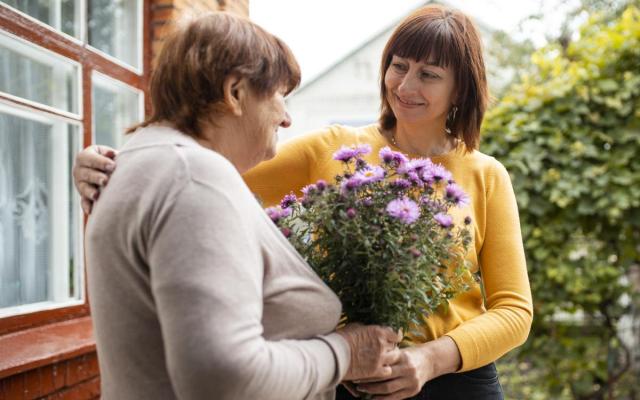 een dame schenkt een boeket bloemen aan haar oudere buurvrouw