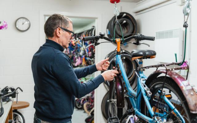 een vrijwilliger sleutelt aan een tweedehands kinderfiets in de Fietsbieb in 't Kattegat, Wuustwezel