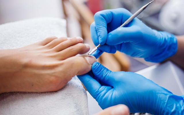 close-up van een pedicure met blauwe handschoenen en een voet die wordt verzorgd