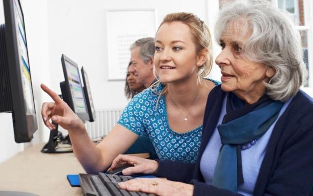 een jonge vrouw geeft computerles aan een oudere vrouw