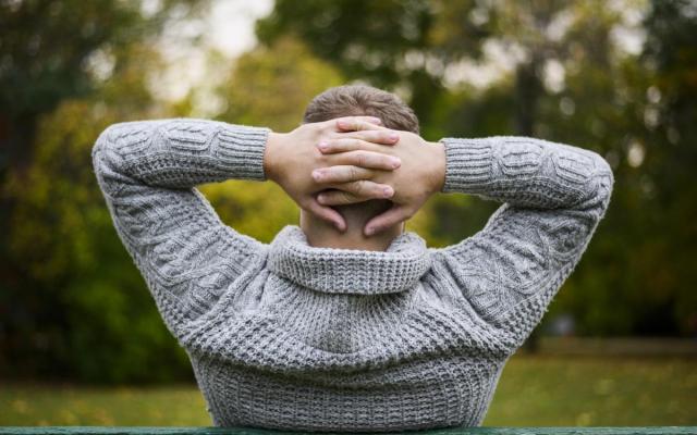 een man zit op een bankje in het park en houdt zijn handen achter zijn hoofd