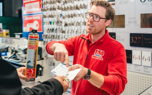 een klant en een medewerker in Hubo wisselen spaarzegels van de Wuustwezelse eindejaarsactie uit aan de kassa