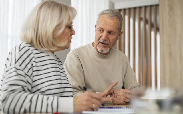een oudere dame en man aan een tafel met schrijfgerief