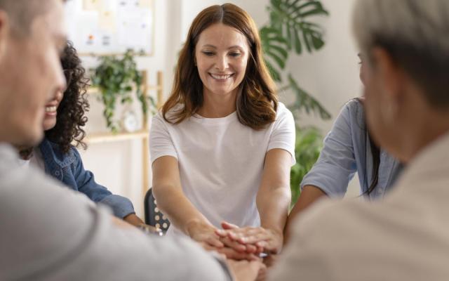 een vrouw houdt handen voor zich samen met een groepje collega's als een uiting van verbinding en teambuilding