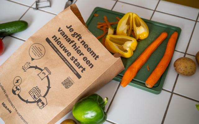 een papieren keukenafvalzakje bij een snijplank met verschillende groenten