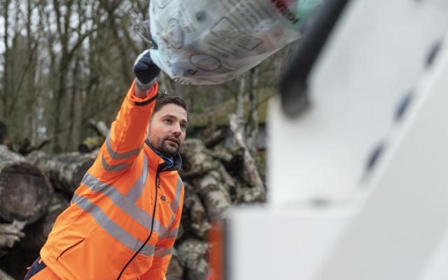 een medewerker van Igean werpt een volle pmd-zak in een afvalwagen