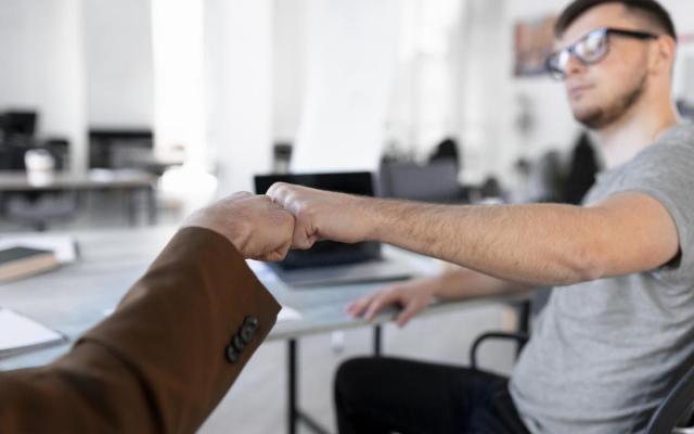 een jongere en oudere man geven elkaar een vuistje in een kantooromgeving