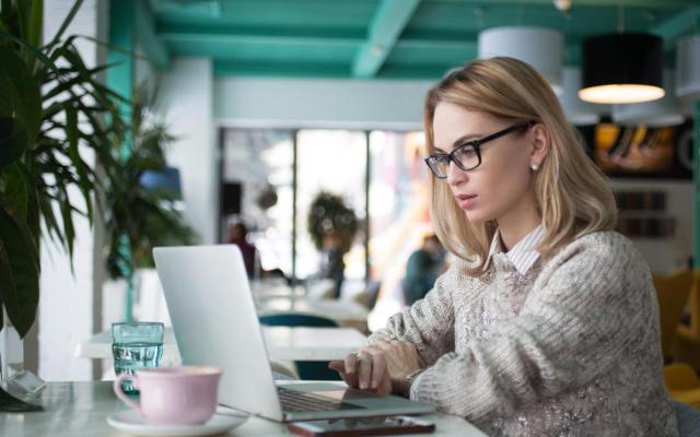 een vrouw zit aan een tafel en typt op een laptop