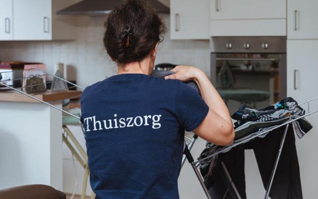 een verzorgende van de Wuustwezelse thuiszorgdienst strijkt kleren thuis bij een cliënt