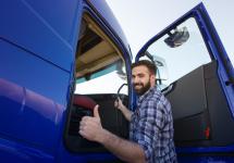 een truckchauffeur lacht en steekt z'n duim omhoog bij zijn vrachtwagen