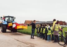 Een groepje schoolkinderen van het vierde leerjaar krijgt uitleg over hoe veilig fietsen langs landbouwvoertuigen