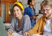 een glimlachende vrouw zit aan een tafel met enkele collega's