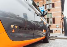 grijze elektrische deelauto met het logo van de gemeente Wuustwezel aan het Wuustwezelse gemeentehis