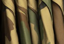 vijf camouflage uniformen hangend aan een kapstok