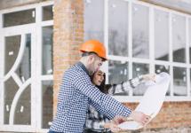 een architect staat voor een nieuwbouw en bekijkt bouwplannen