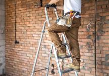 een elektricien aan het werk op een laddertje in een bouwwerf