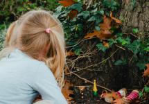 een meisje kijkt naar kleine houten kaboutertjes onder een boom
