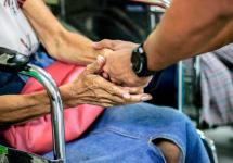 Een hand van een volwassene houdt een hand van een oudere dame vast